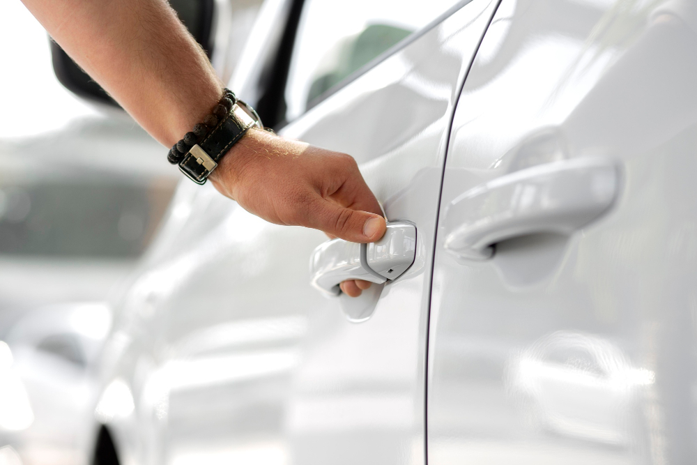 Main ouvrant portière de voiture blanche.